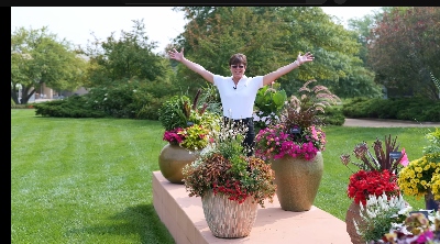 Excited woman standing outside among a variety of flower containers